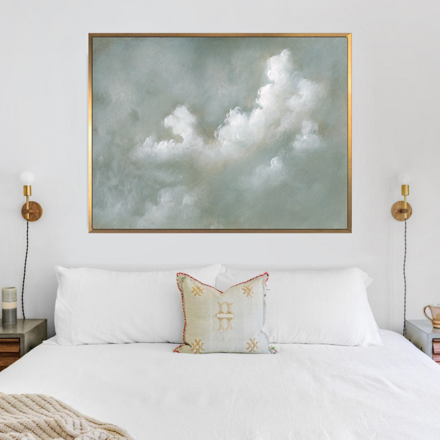 Framed artwork of clouds above a bed with decorative pillows.